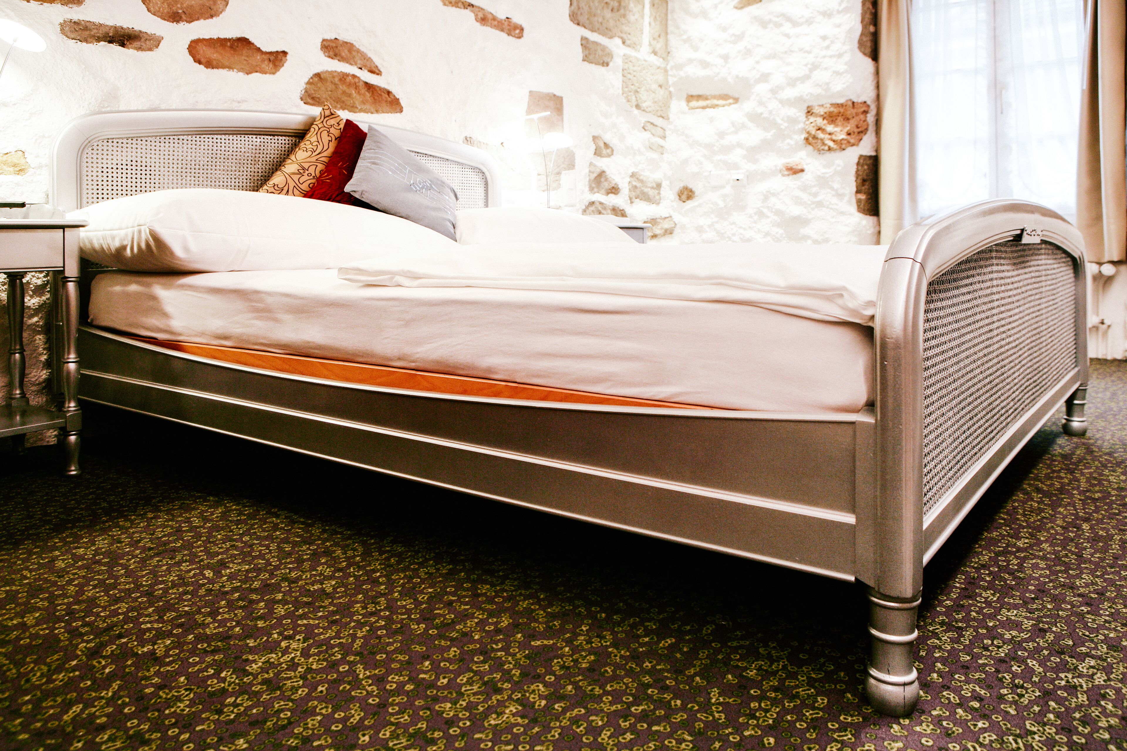 Ein Bett mit Metallgestell, einem weißen Kopfteil und einem gemusterten Teppich.