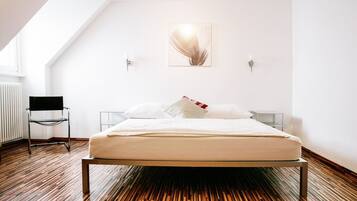 Camera da letto moderna con soffitto spiovente, un letto con lenzuola bianche, una sedia nera e un punto luce a parete.