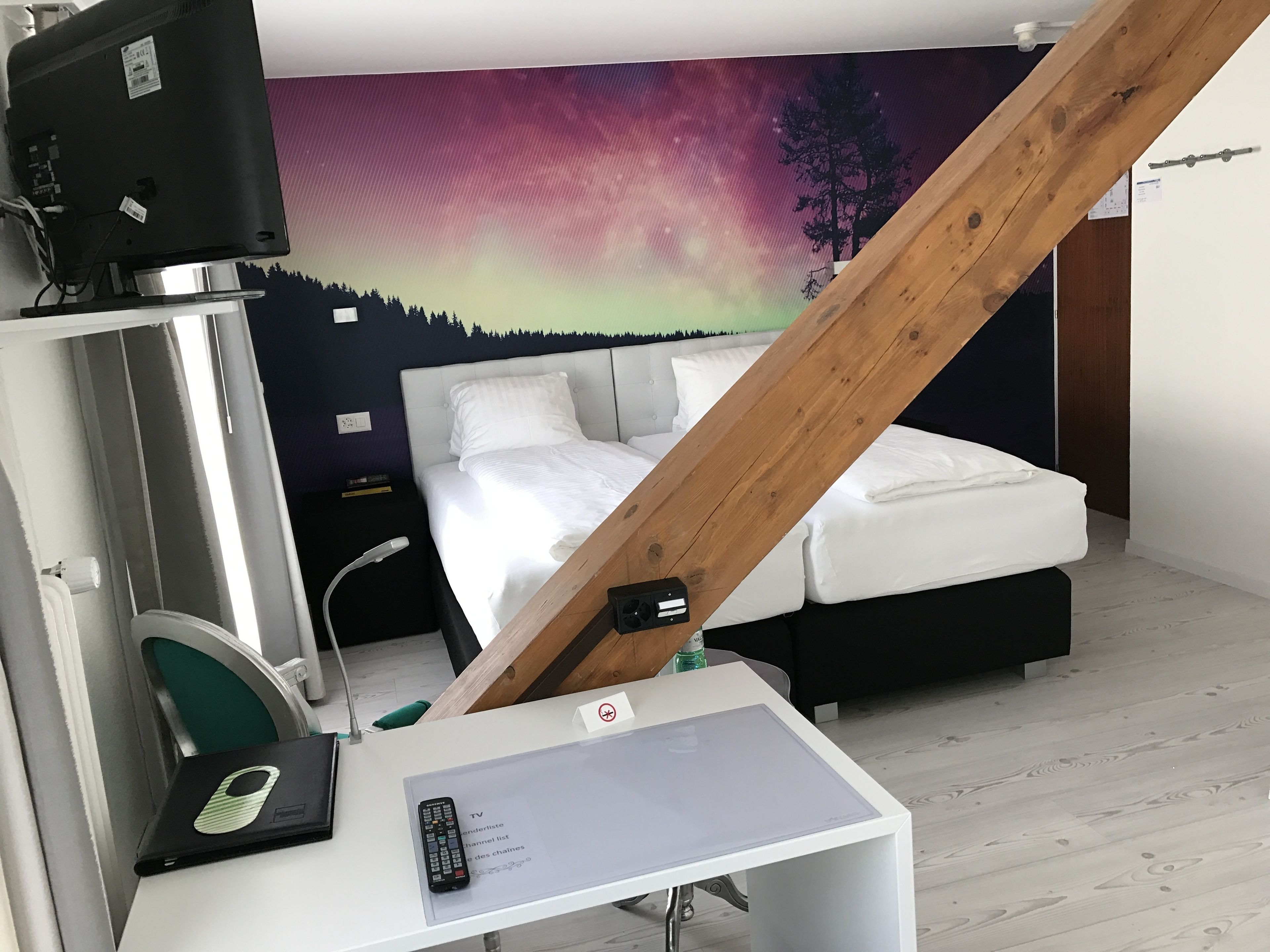 Un dormitorio con cama, un escritorio con computadora portátil, un televisor y un mural en la pared.