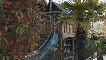 Un parque infantil con un tobogán, rodeado de árboles y una valla.