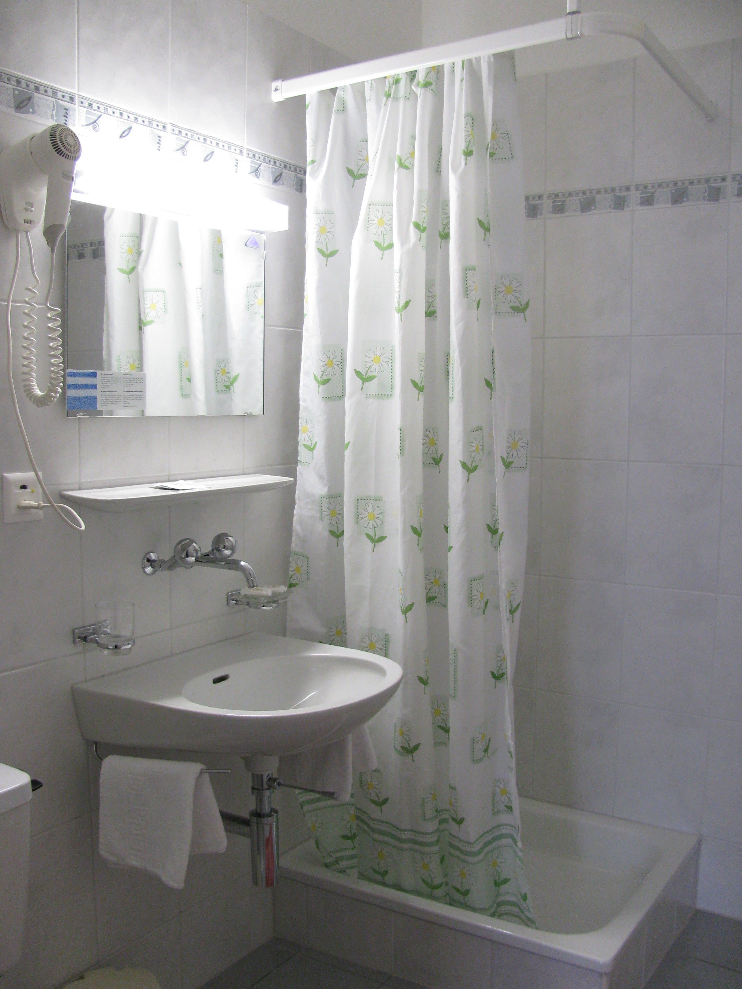 Un baño con lavamanos blanco, un espejo, un secador de pelo y una cortina de ducha con estampado floral.