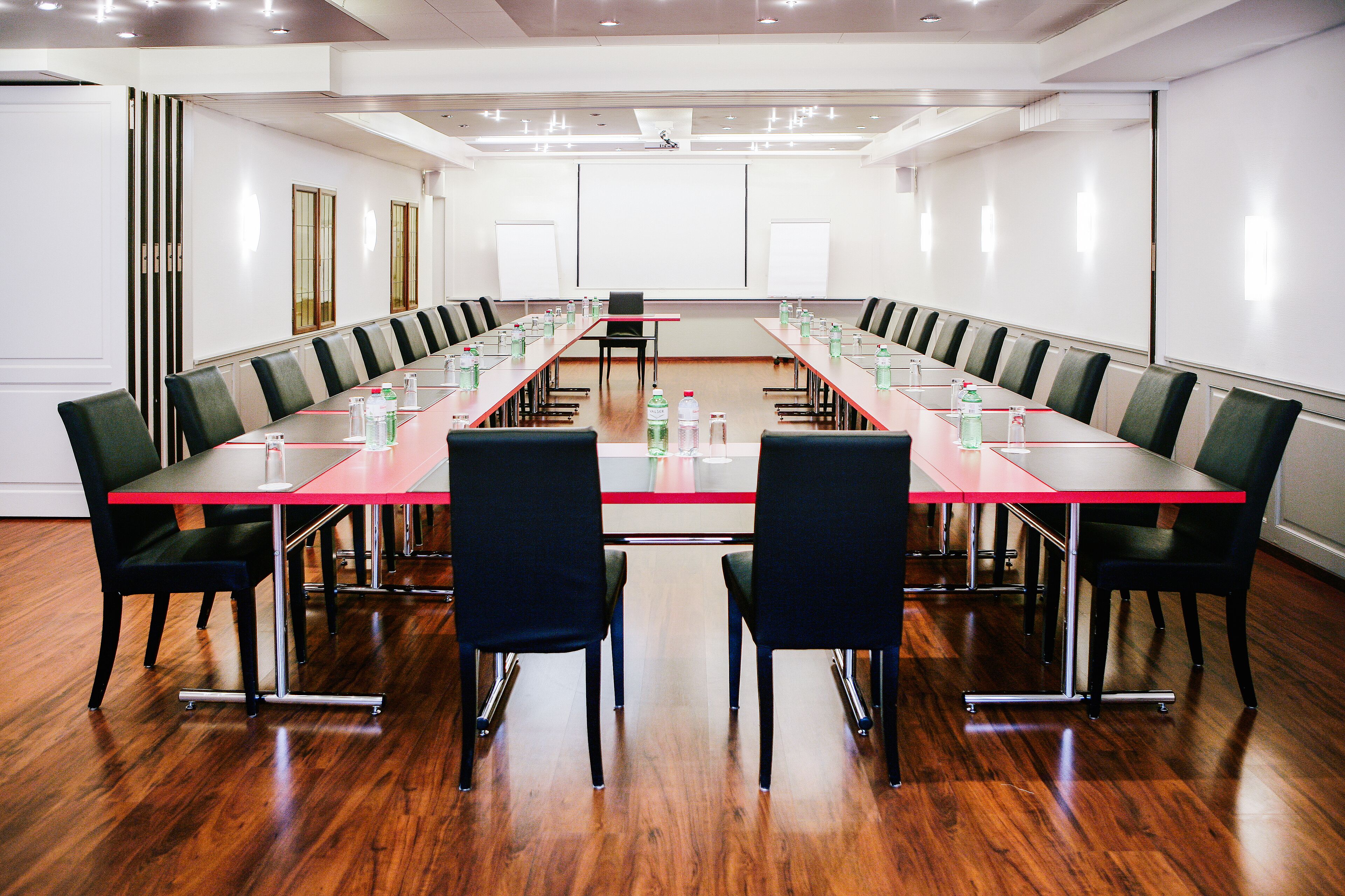 A conference room with a long table, chairs, and a projector screen.