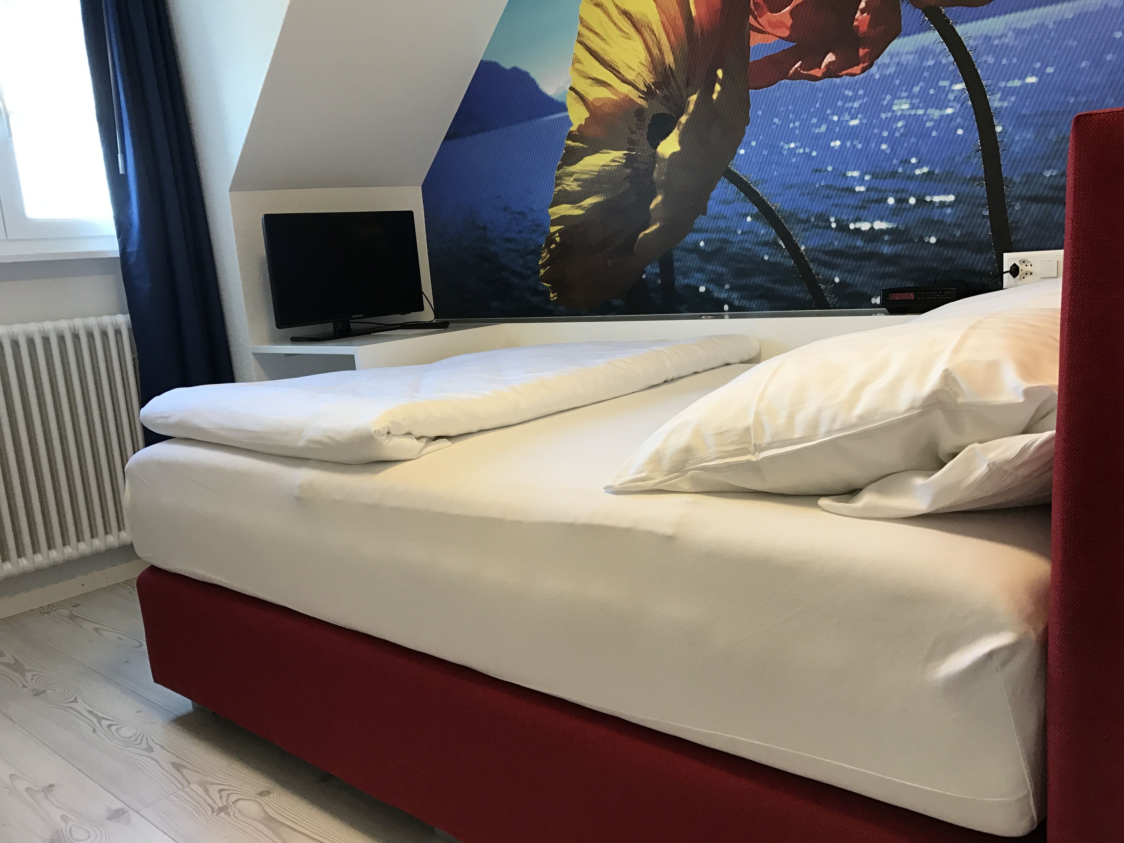 A bed with white bedding, a red headboard, and a wall-mounted TV.