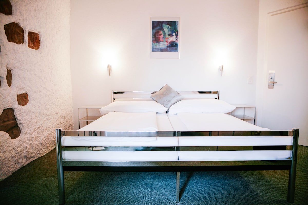 Una habitación de hotel moderna con estructura de cama de metal, ropa de cama blanca y pared de piedra.