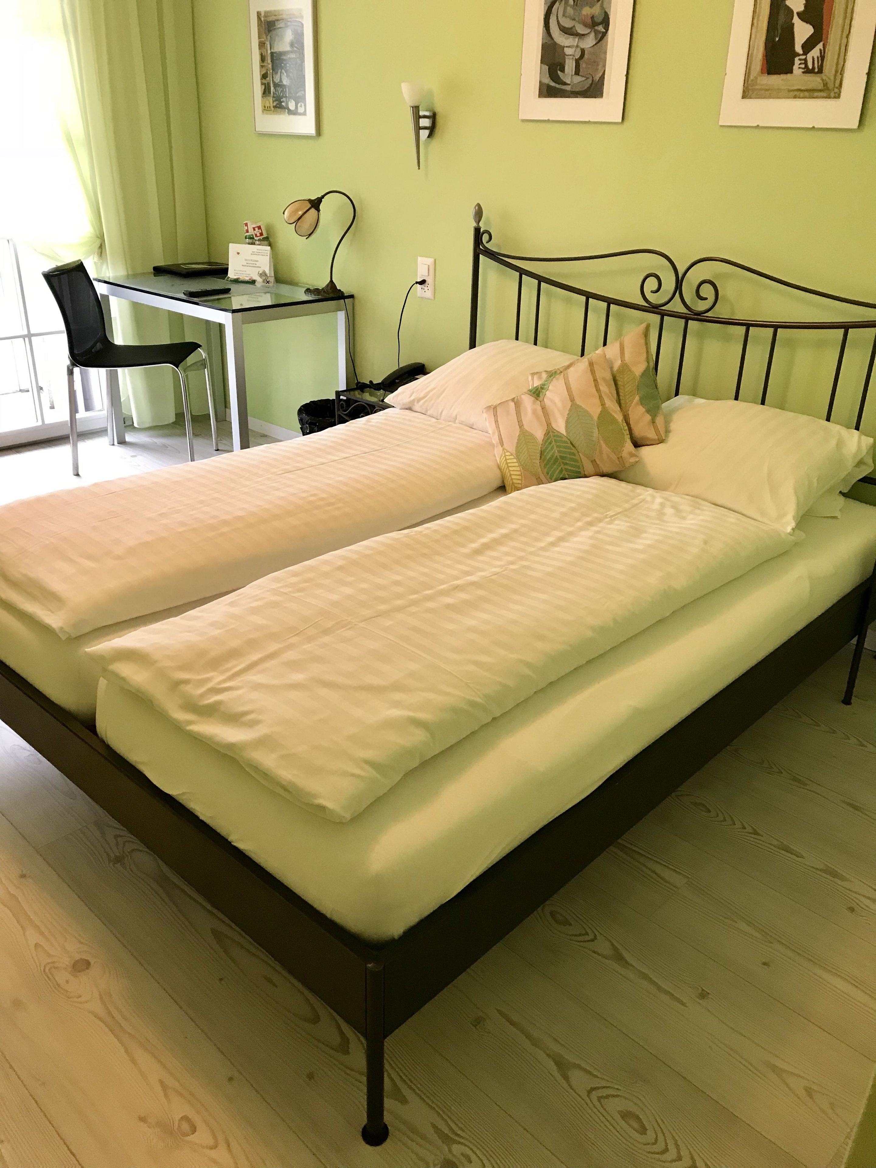 A room with two single beds, a desk with a chair, and a window with curtains.