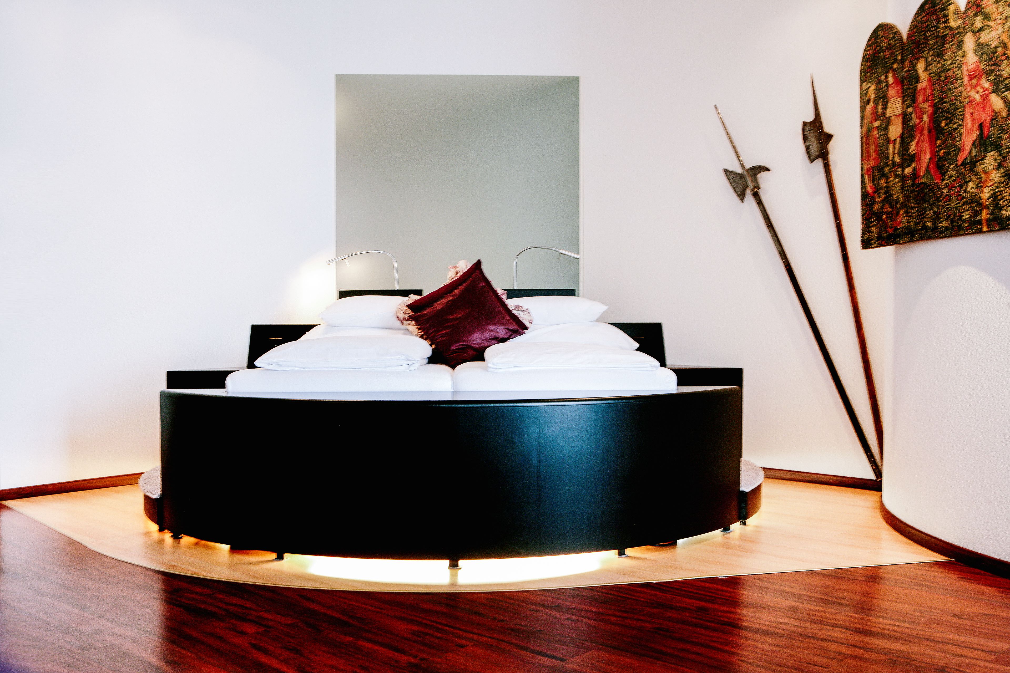 A modern bedroom with a round bed, a large mirror, and a painting on the wall.