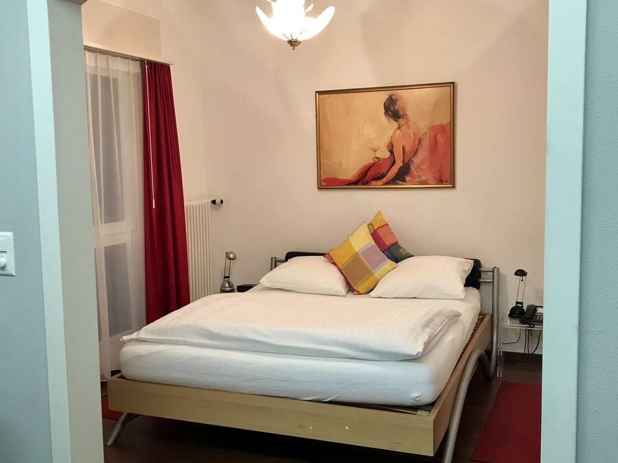 A bedroom with a bed, a painting, a nightstand, and a lamp.