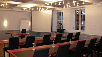 Ein Konferenzraum mit mehreren Tischen und Stühlen, einer Projektionsleinwand und einem Fenster mit Blick nach außen.