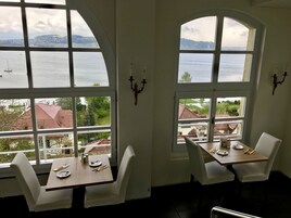 A dining area with two tables and chairs, large arched windows with a view of a body of water and buildings.
