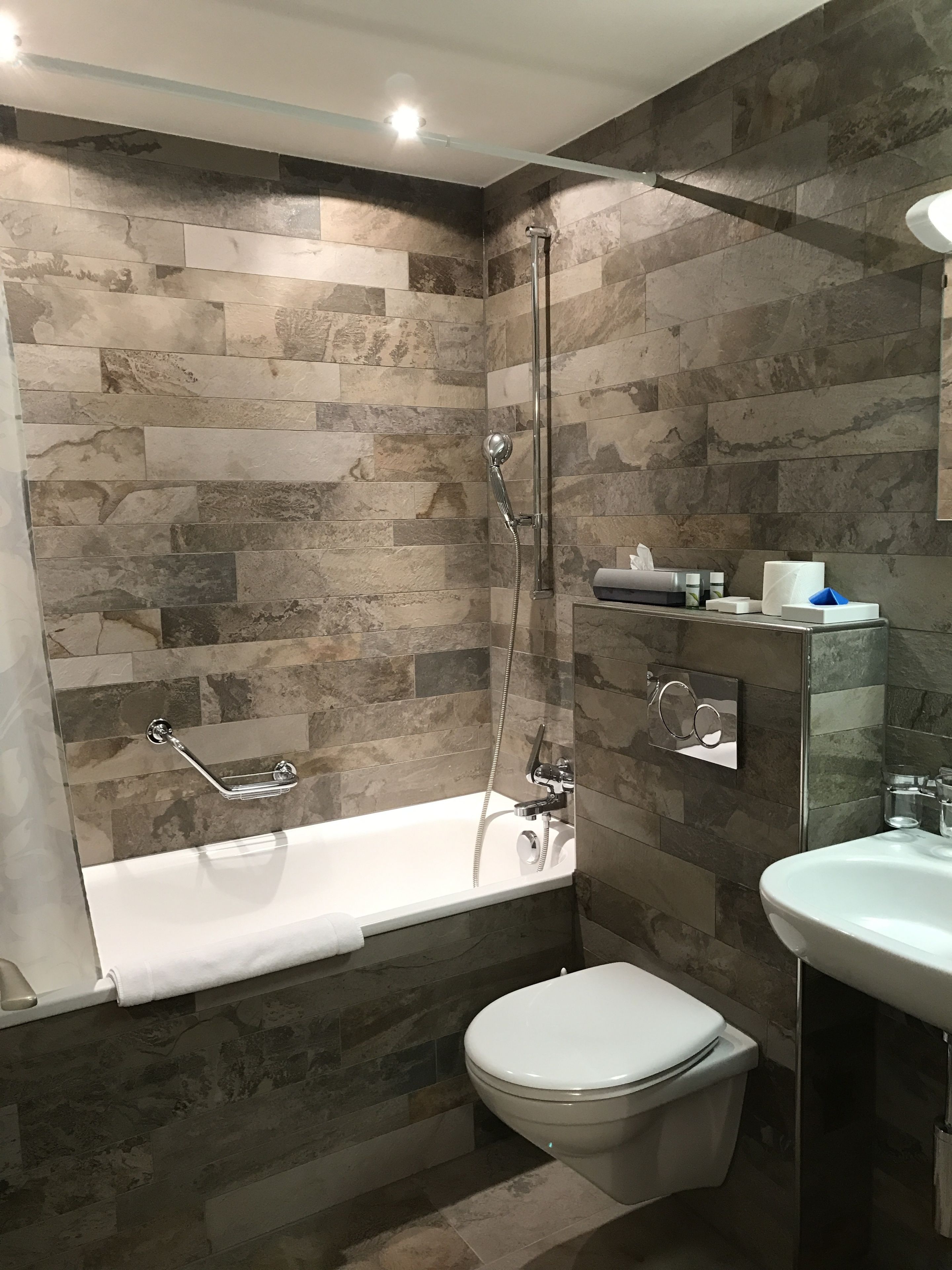Un baño moderno con bañera, inodoro y lavamanos, todo con accesorios de cromo.