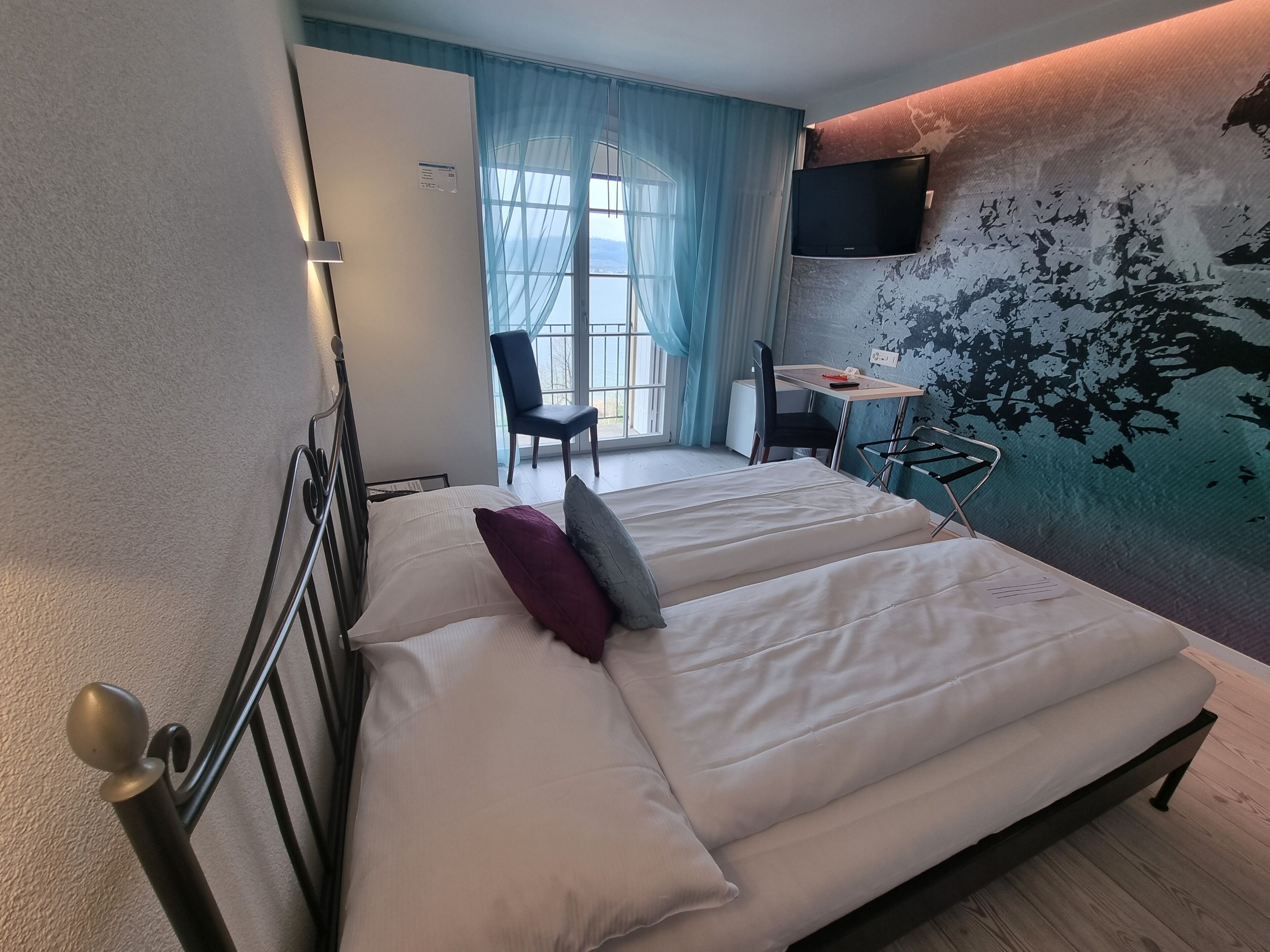 Una habitación de hotel con una cama, un escritorio, una silla, un televisor y una ventana con cortinas.