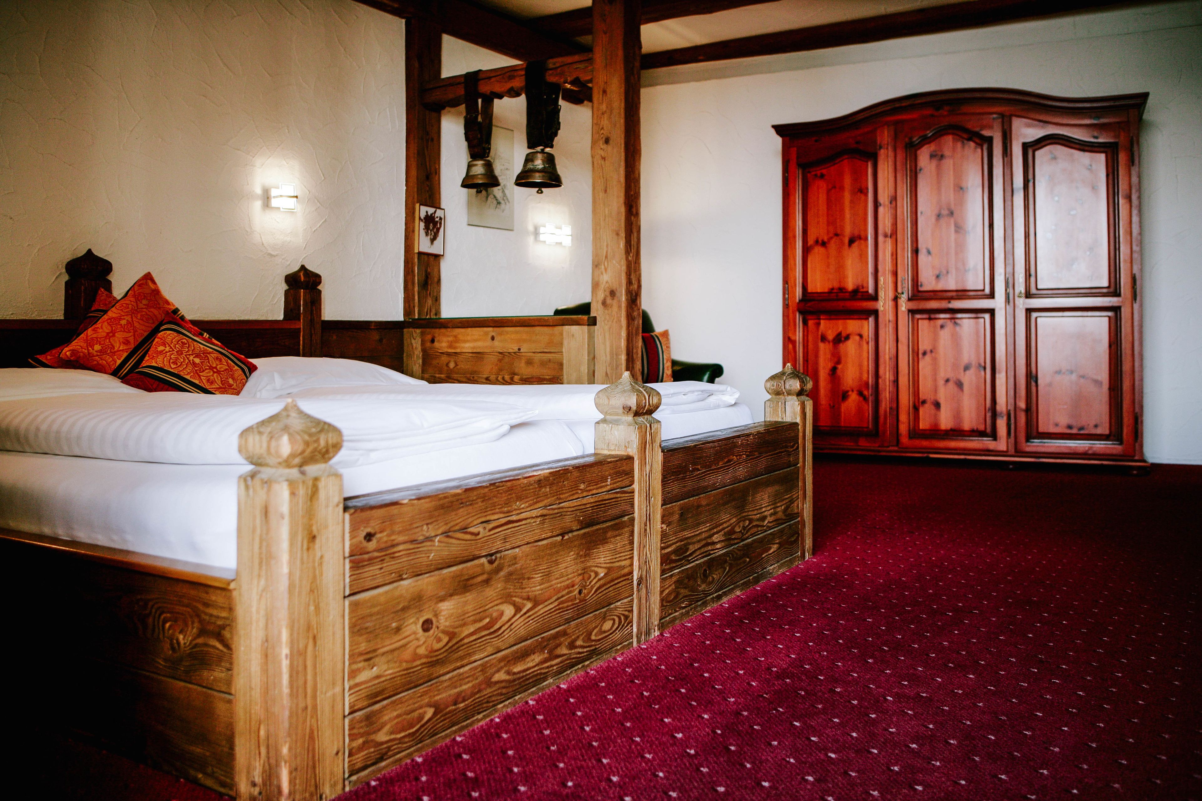 A wooden bed with a headboard, a red carpet, and a wooden wardrobe in a room.