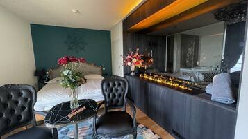 Una habitación de hotel moderna con una cama, un escritorio con silla, un florero y un espejo que refleja la habitación.