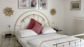 Ein ordentlich eingerichtetes Schlafzimmer mit einem weißen Metallbettgestell, einem Nachttisch mit Lampe und blumengeschmückten Wanddekorationen.