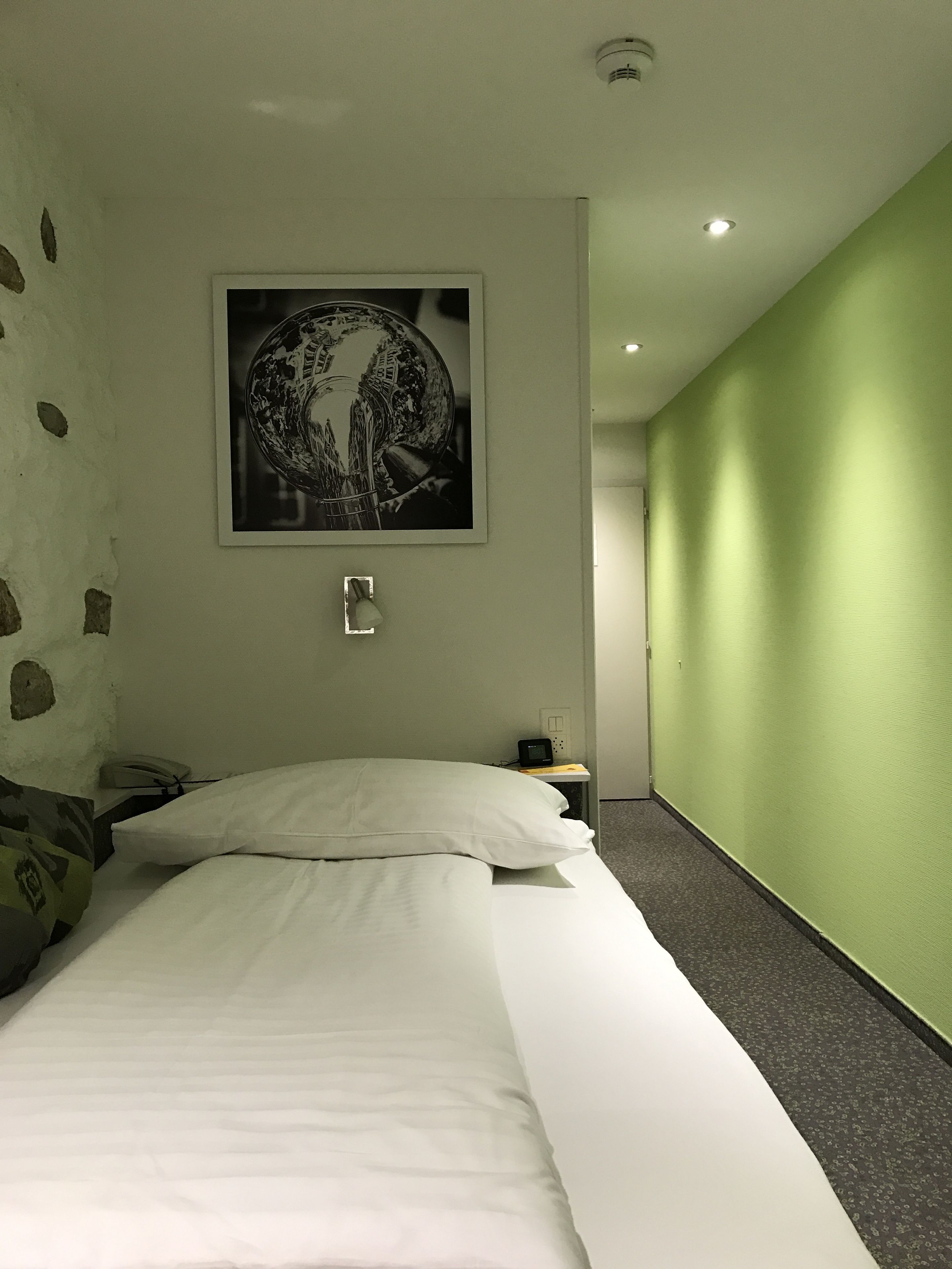 Une chambre d’hôtel avec un lit, une table de chevet, une lampe, un téléphone et un tableau accroché au mur.