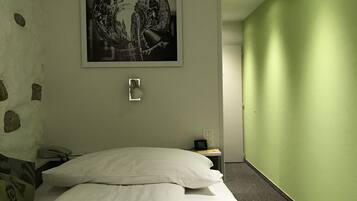 Une chambre d’hôtel avec un lit, une table de chevet, une lampe, un téléphone et un tableau accroché au mur.