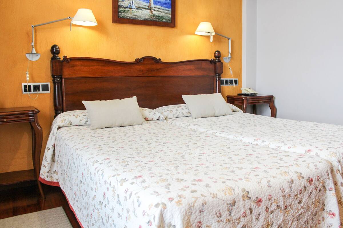 Una cama doble con cubrecama floral, dos lámparas de noche y un cuadro sobre el cabecero.