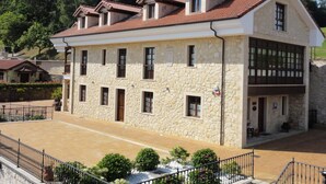 A stone building with multiple windows and a tiled roof, surrounded by a paved area and greenery. - Mirador de Moriyón (Villaviciosa)