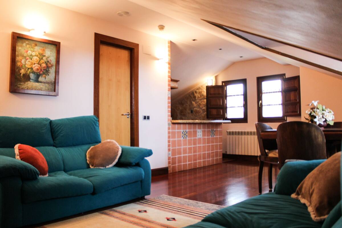 Una sala de estar acogedora con un sofá azul turquesa, una puerta de madera y una zona de cocina con salpicadero de piedra.