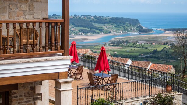A terrace with wooden chairs and red umbrellas, overlooking a coastal landscape with a view of the sea and hills. - Mirador de Moriyón (Villaviciosa)