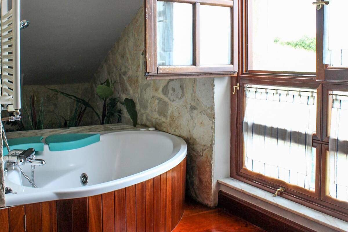 Un baño con tocador de madera, bañera y ventana con vistas a la vegetación.