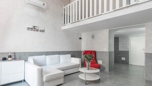 Een moderne woonkamer met een witte bank, een rode fauteuil, een kleine tafel en een balkon.