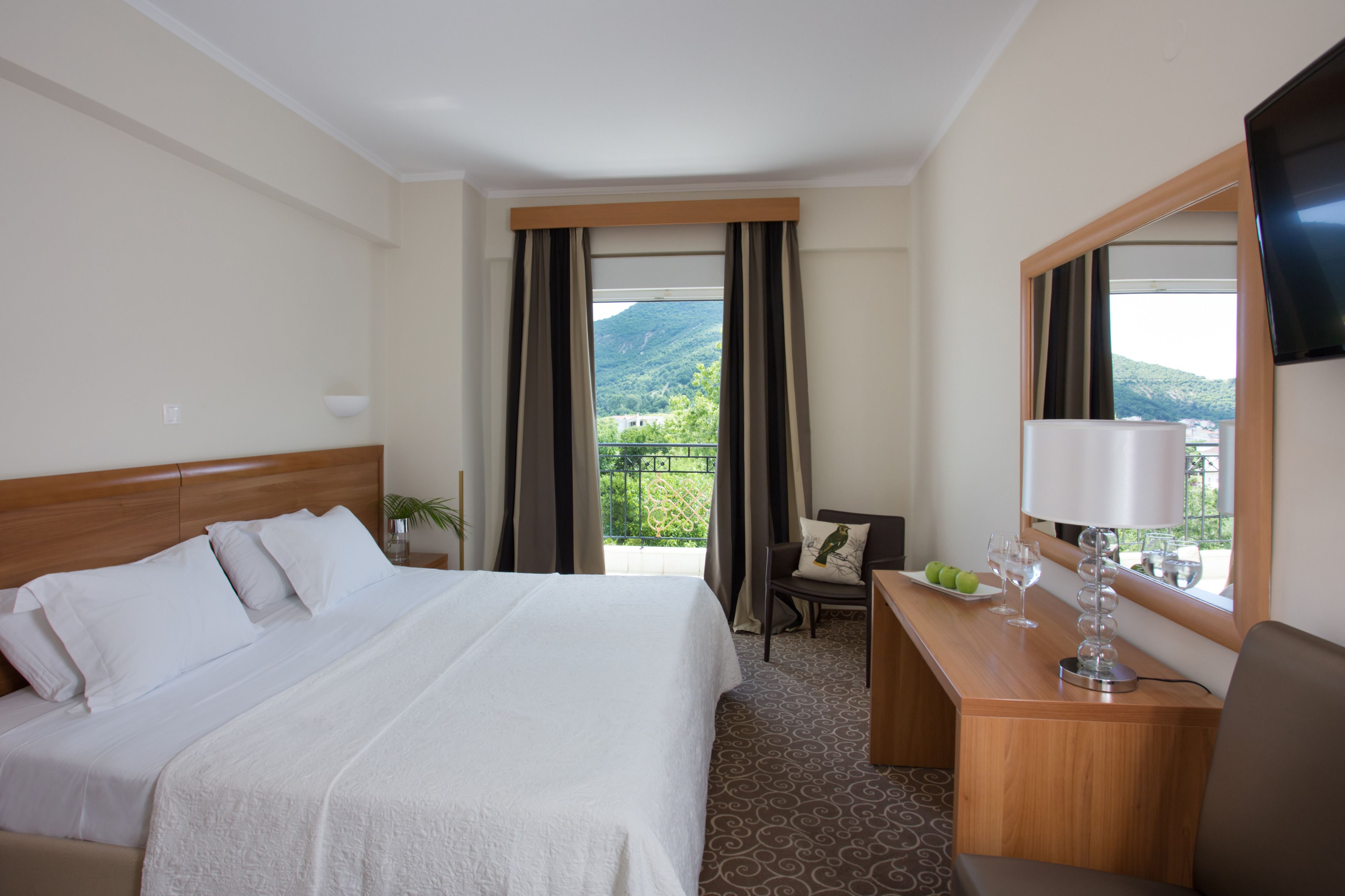 Una habitación de hotel con una cama grande, un escritorio con lámpara, una silla y un televisor.