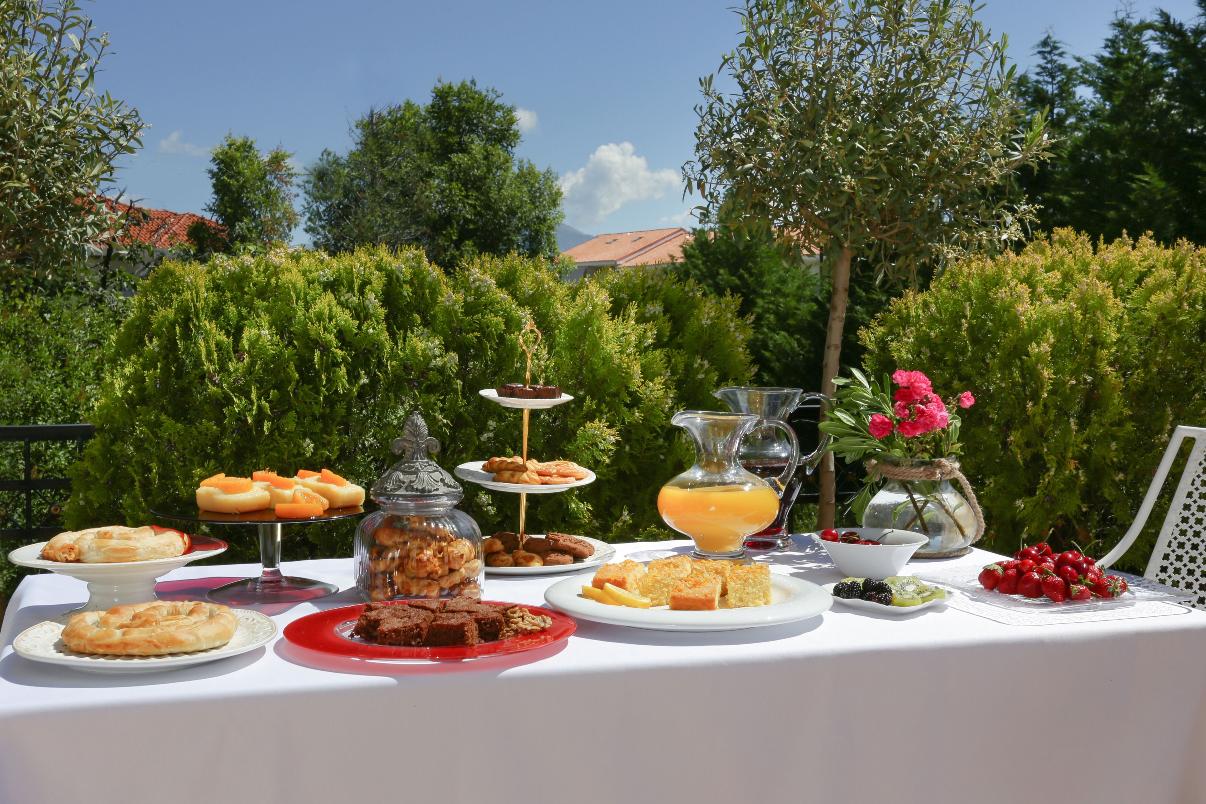 Buffet ao ar livre com diversos alimentos e uma jarra de suco de laranja.