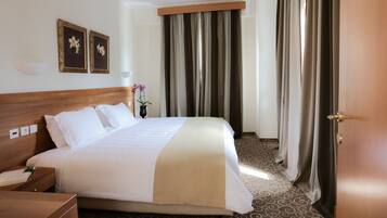 A hotel room with a large bed, a wooden headboard, two framed pictures on the wall, a nightstand, a lamp, and a window with curtains.
