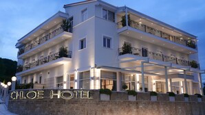 Un hotel de varios pisos con balcones, una entrada bien iluminada y una pared de piedra con el nombre del hotel.