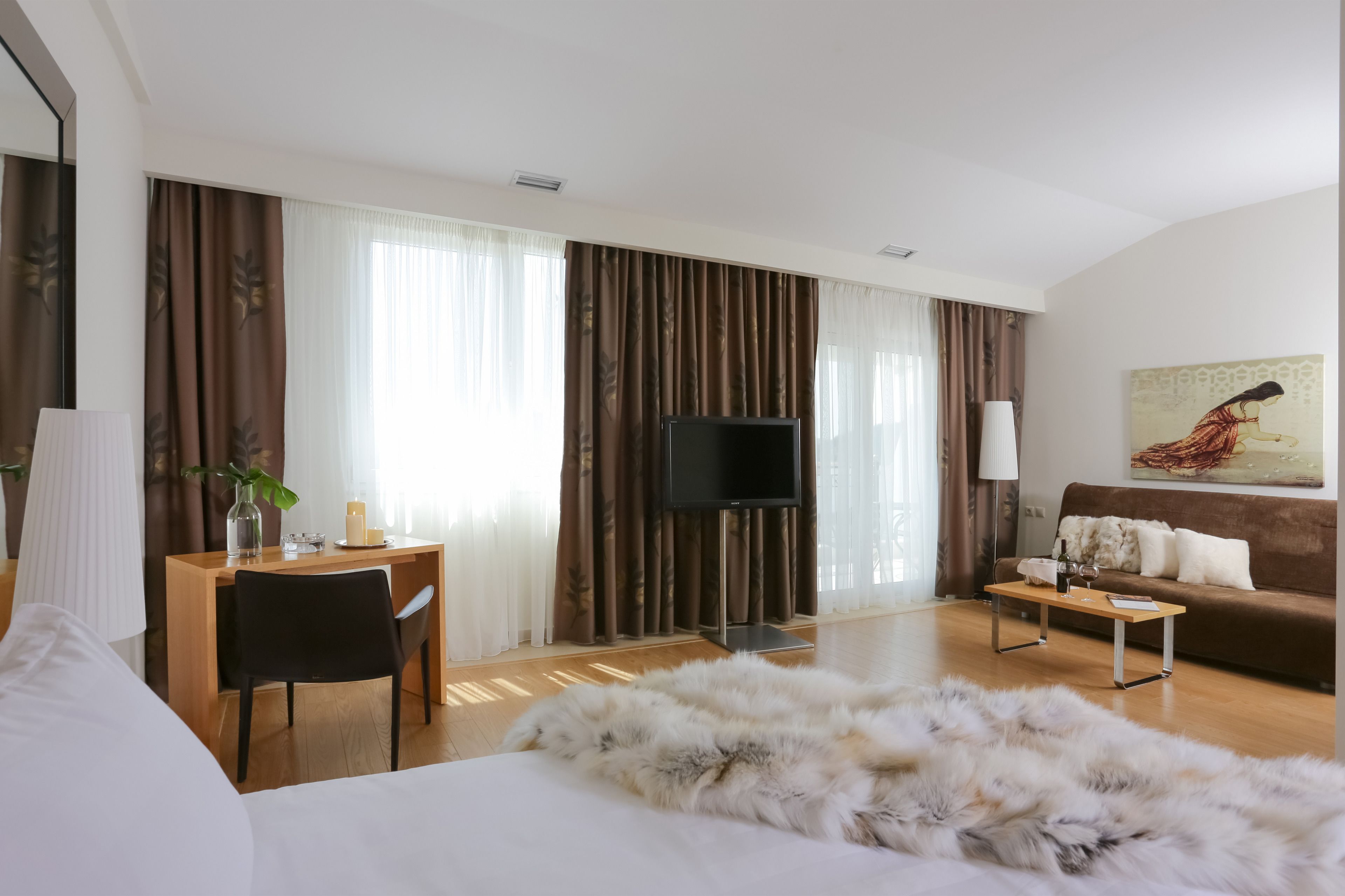 Una habitación de hotel moderna con una cama grande, un escritorio de madera, un televisor, un sofá y un cuadro en la pared.