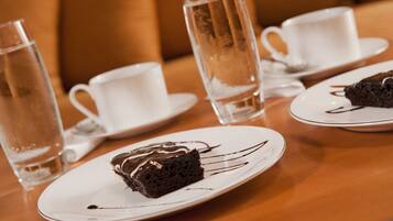 A table with a slice of chocolate cake on a white plate, a tall glass of water, and a white cup on saucer.