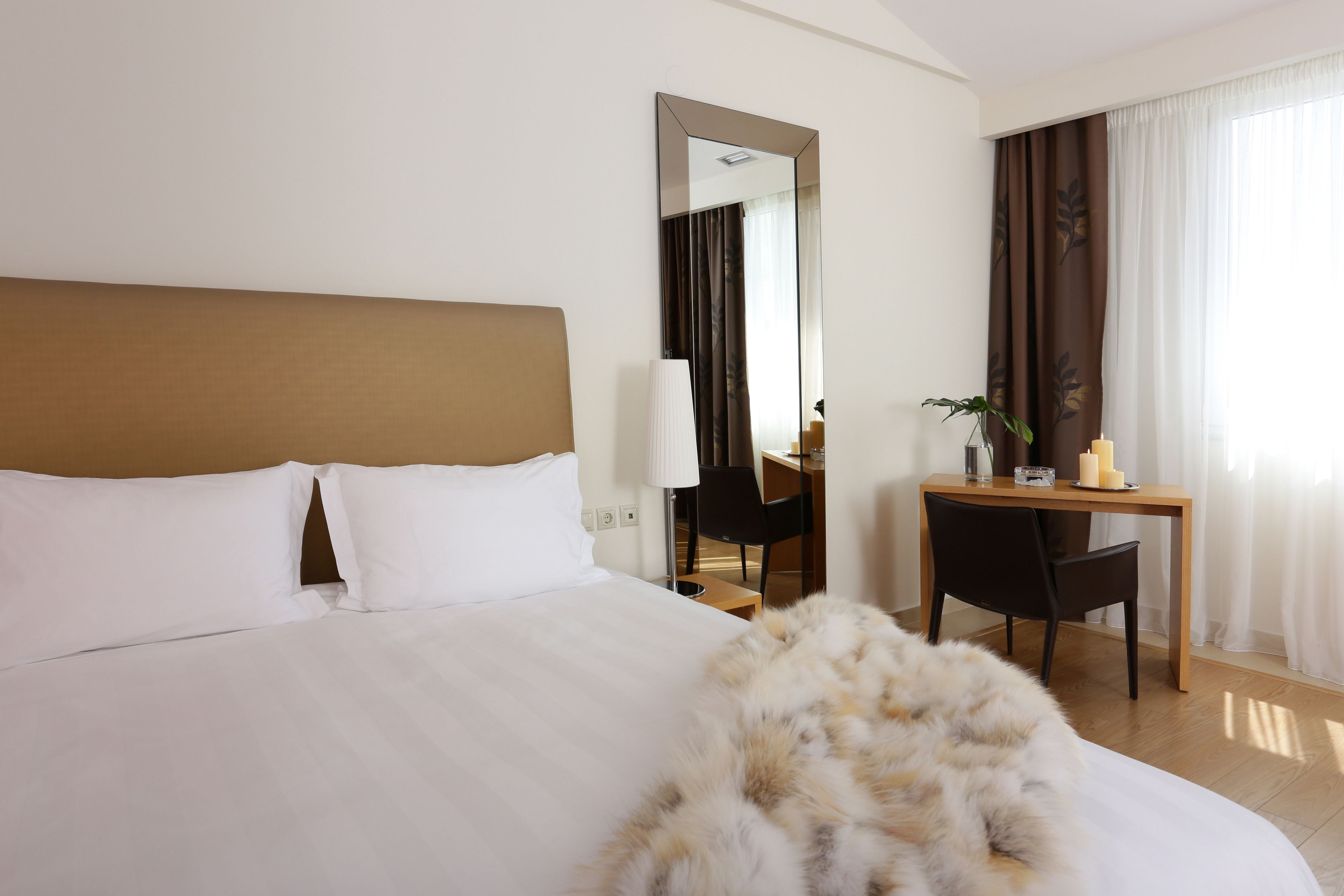 A hotel room with a large bed, a desk, a chair, and a mirror.