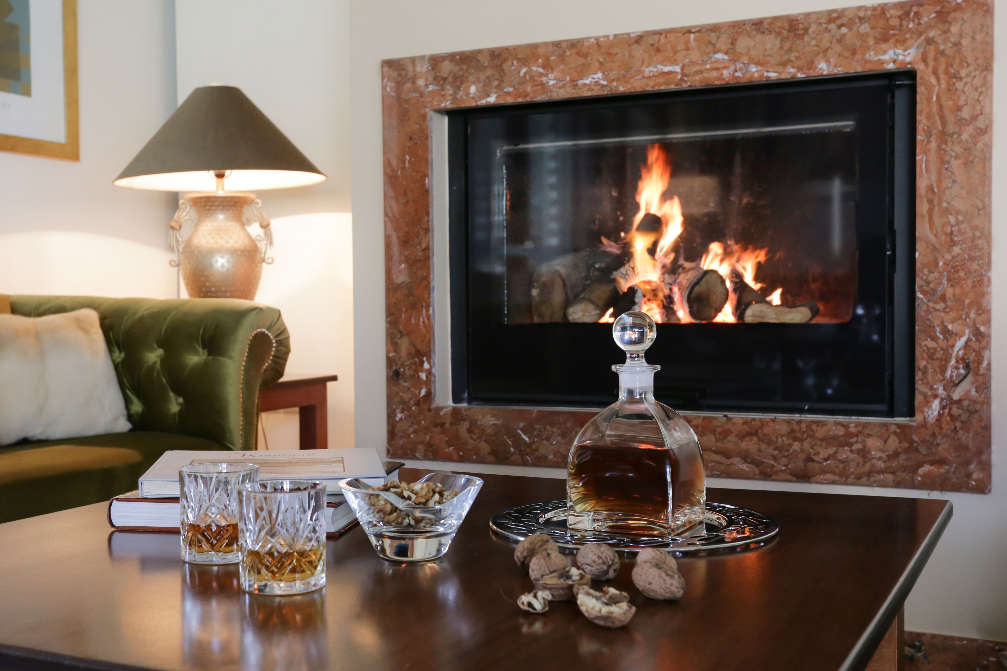 A cozy living room with a fireplace, a green sofa, a table with glasses, a bowl of nuts, and a bottle of liquor.