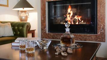 A cozy living room with a fireplace, a green sofa, a table with glasses, a bowl of nuts, and a bottle of liquor.