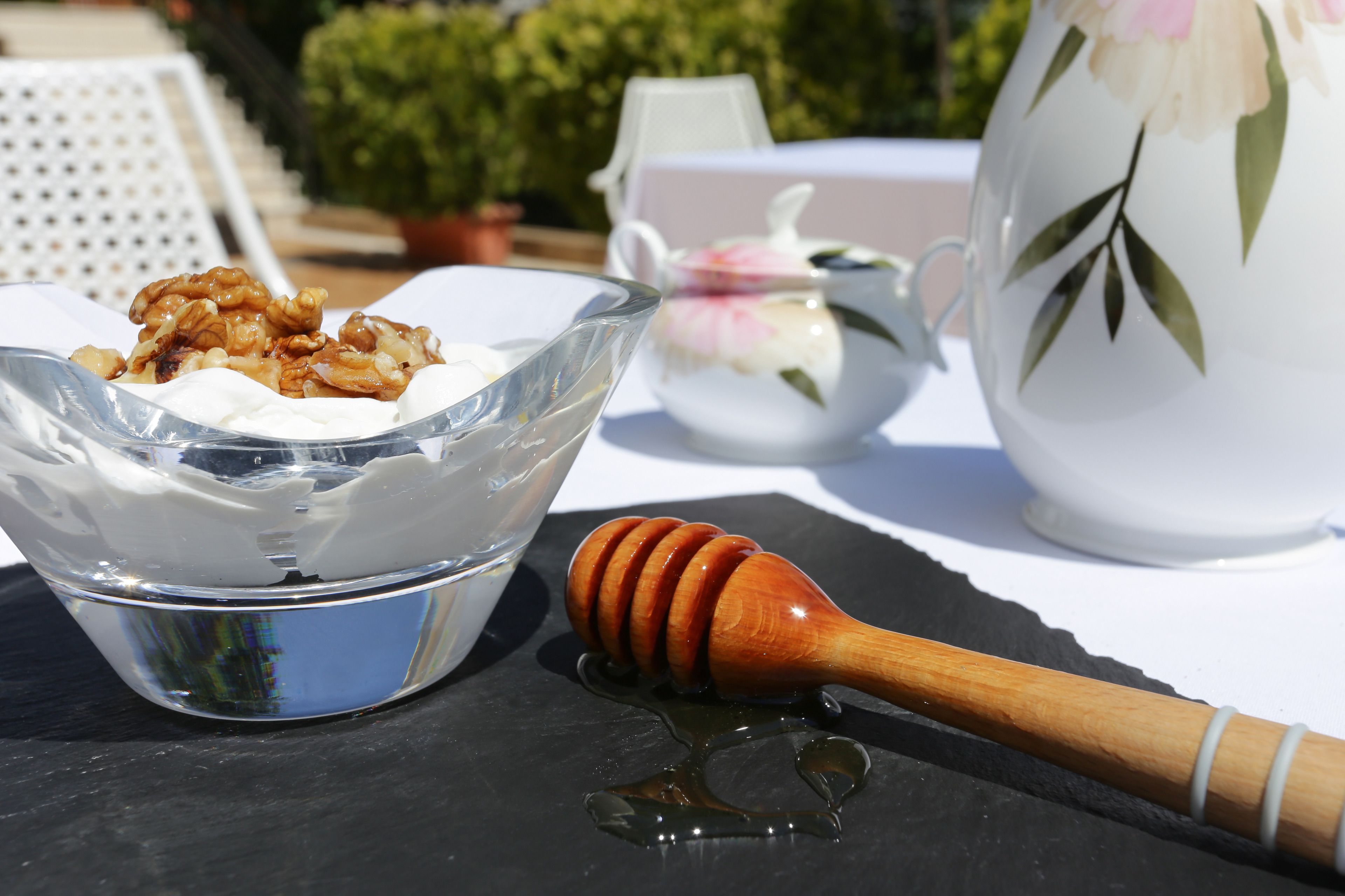 A clear glass bowl with a white substance and walnuts, a honey dipper with honey, and a floral teapot on a table.