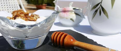 Un tazón de vidrio transparente con una sustancia blanca y nueces, un cucharón de miel con miel, y una tetera decorada con flores sobre una mesa.