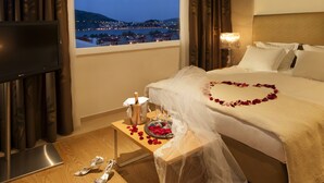 Una habitación de hotel con cama, televisor, mesita de noche con una botella de champán, copas y un par de zapatos.