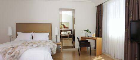 Una habitación de hotel moderna con una cama grande, un escritorio, una silla, un televisor y un espejo.