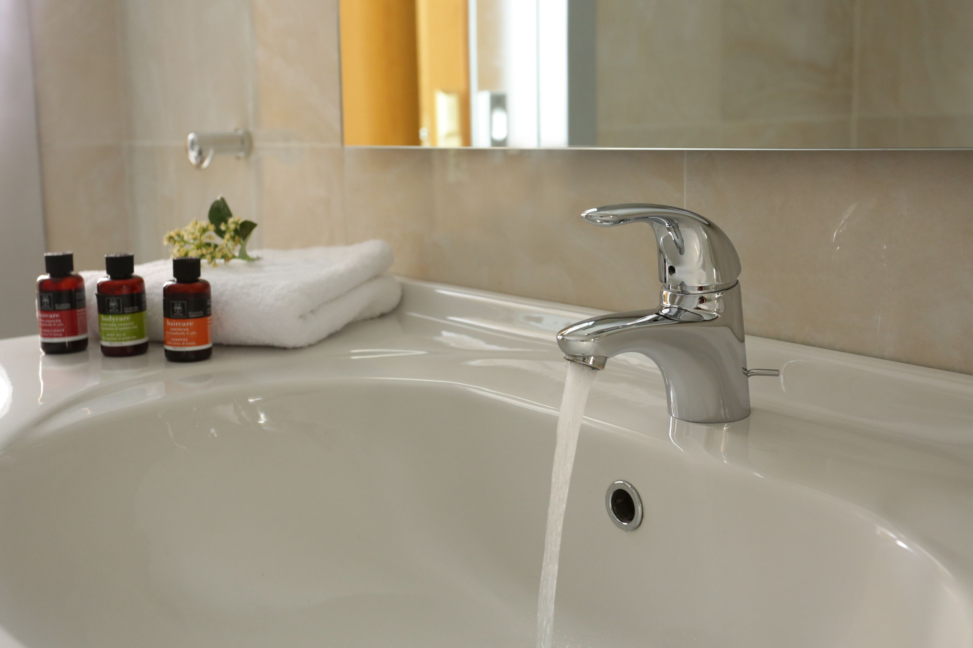 A bathroom sink with a chrome faucet, a white towel, and three bottles of toiletries.