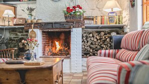 Una sala de estar acogedora con chimenea, sofá a rayas, mesa de centro de madera y diversos objetos decorativos.