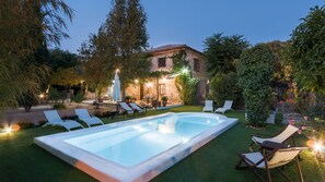 Una piscina con sillones de descanso, un edificio de piedra y follaje circundante.