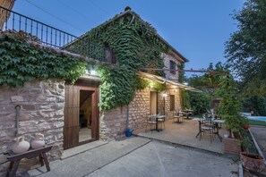 Un edificio de piedra con muros cubiertos de hiedra, asientos al aire libre y un banco de piedra con macetas.