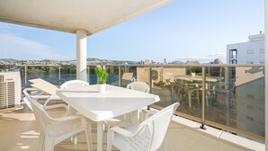 En balkon med et hvidt bord og stole, en potteplante og et gelænder af glas med udsigt over bybilledet.