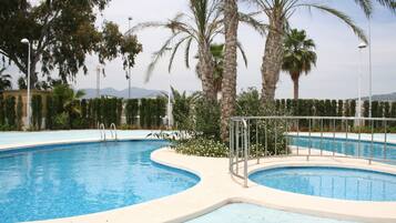 A swimming pool with a curved design, surrounded by palm trees and a metal railing.