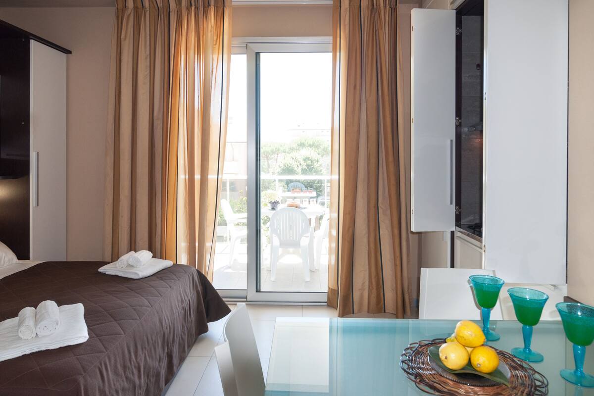 Une chambre d’hôtel avec un lit, une table sur laquelle se trouve un panier de citrons, et un balcon équipé d’une table et de chaises.