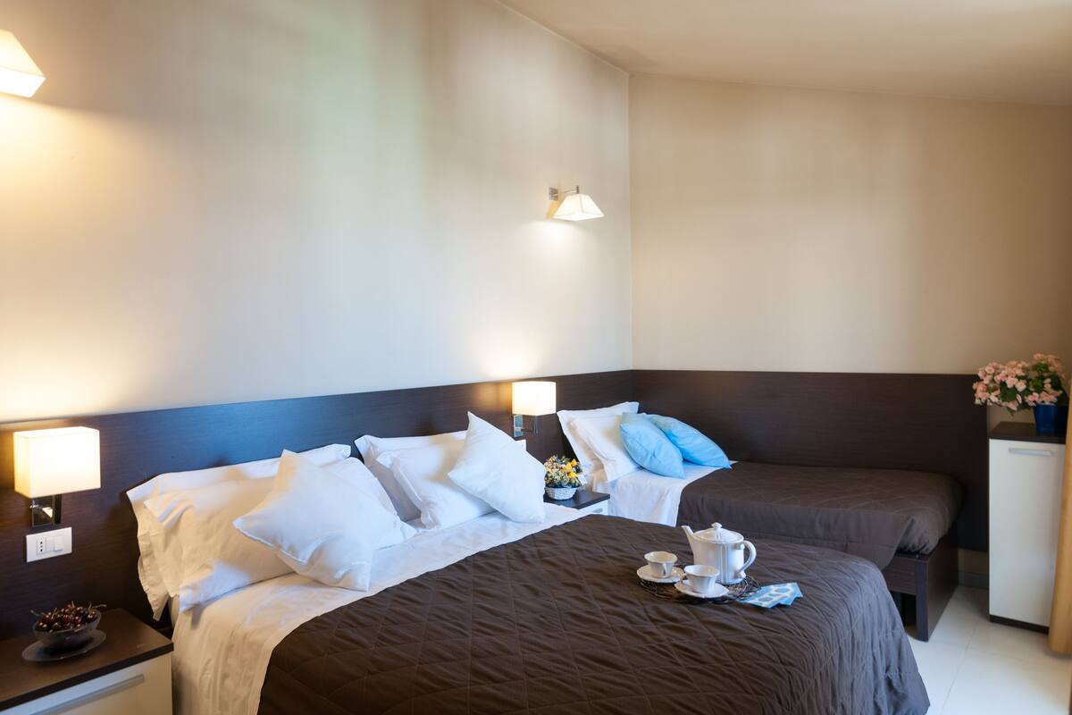 Une chambre d’hôtel avec un grand lit, deux tables de chevet, une petite commode, un petit bureau et une lampe fixée au mur.