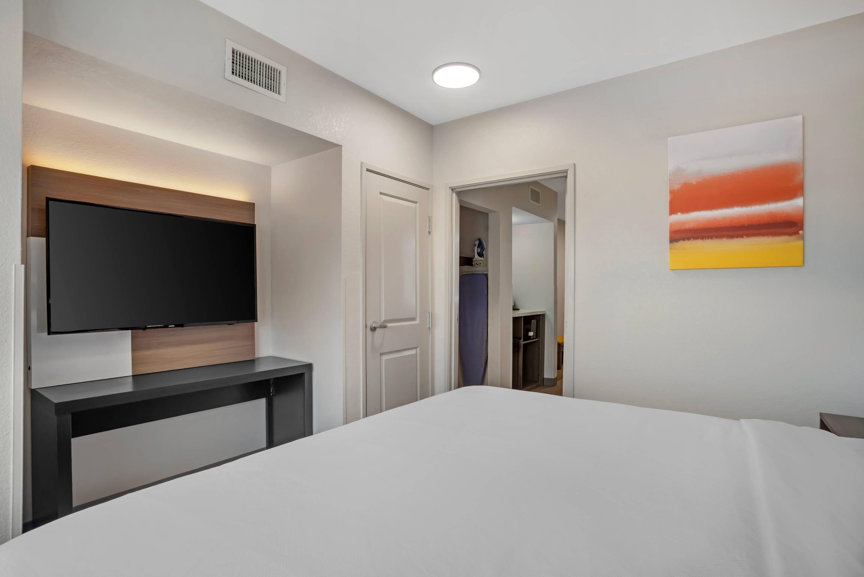 Habitación de hotel con cama, televisor de pantalla plana en la pared, escritorio y un cuadro.