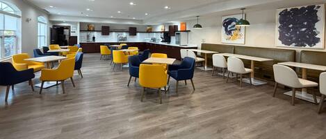 Un espace repas moderne avec plusieurs tables et chaises, une cuisine en arrière-plan et des œuvres d’art accrochées aux murs.