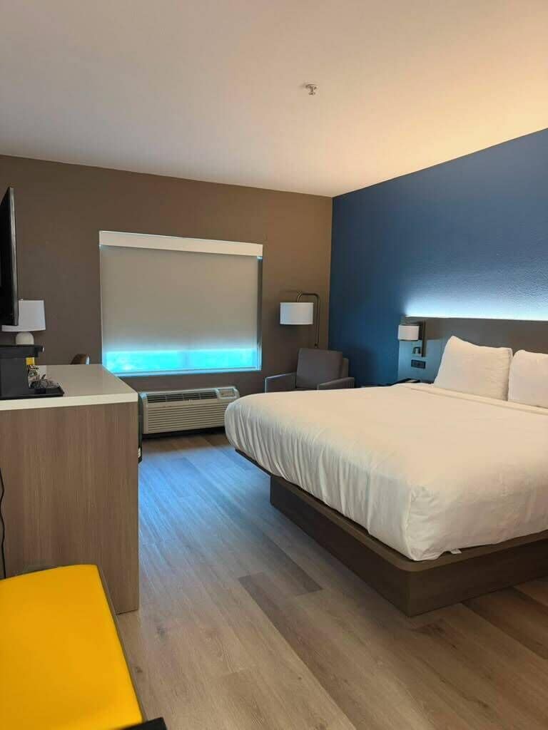 Habitación de hotel con cama, escritorio, silla y ventana con persianas.